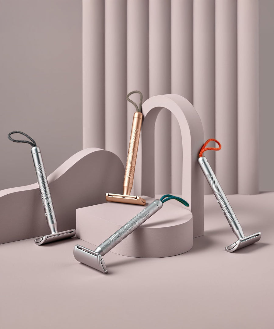 A collection of four MÜHLE Companion Safety Razors on a light pink display and background