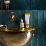 MÜHLE Organic Shaving Cream is stood on a golden sink, next to the MÜHLE Organic Serum, on a blue tiled background