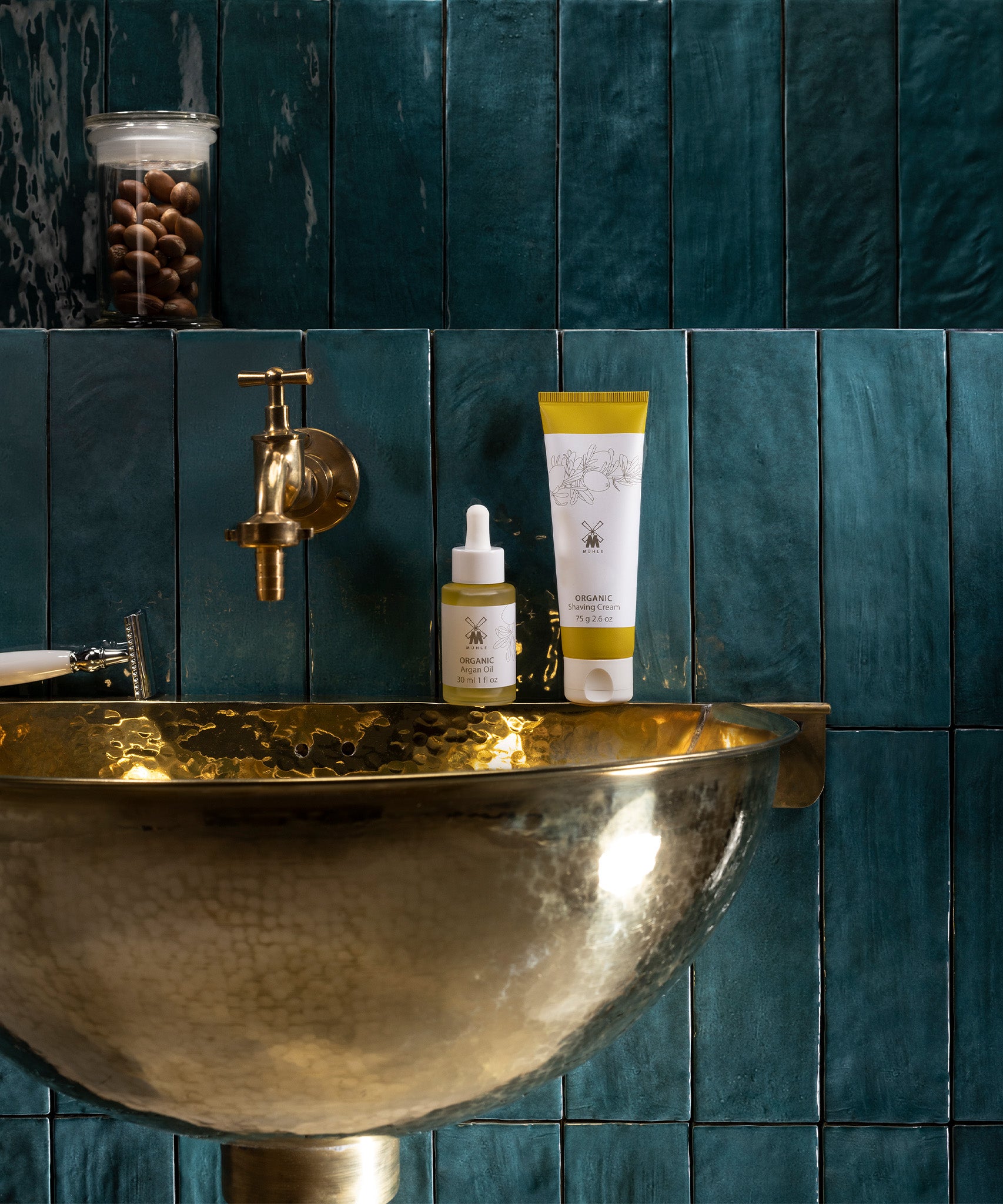 MÜHLE Organic Shaving Cream is stood on a golden sink, next to the MÜHLE Organic Serum, on a blue tiled background