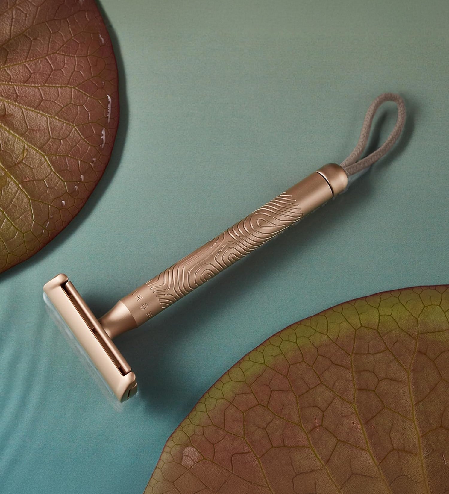 MÜHLE Companion Razor - Rose Gold, is sat on a blue table that looks like water, with two water lilies either side 