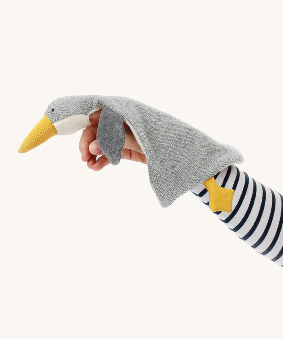 A person has the Nanchen Baby Comforter - Grey Goose resting on their arm, and underneath the head is a small hole to use the comforter as a finger puppet. The image is on a cream background