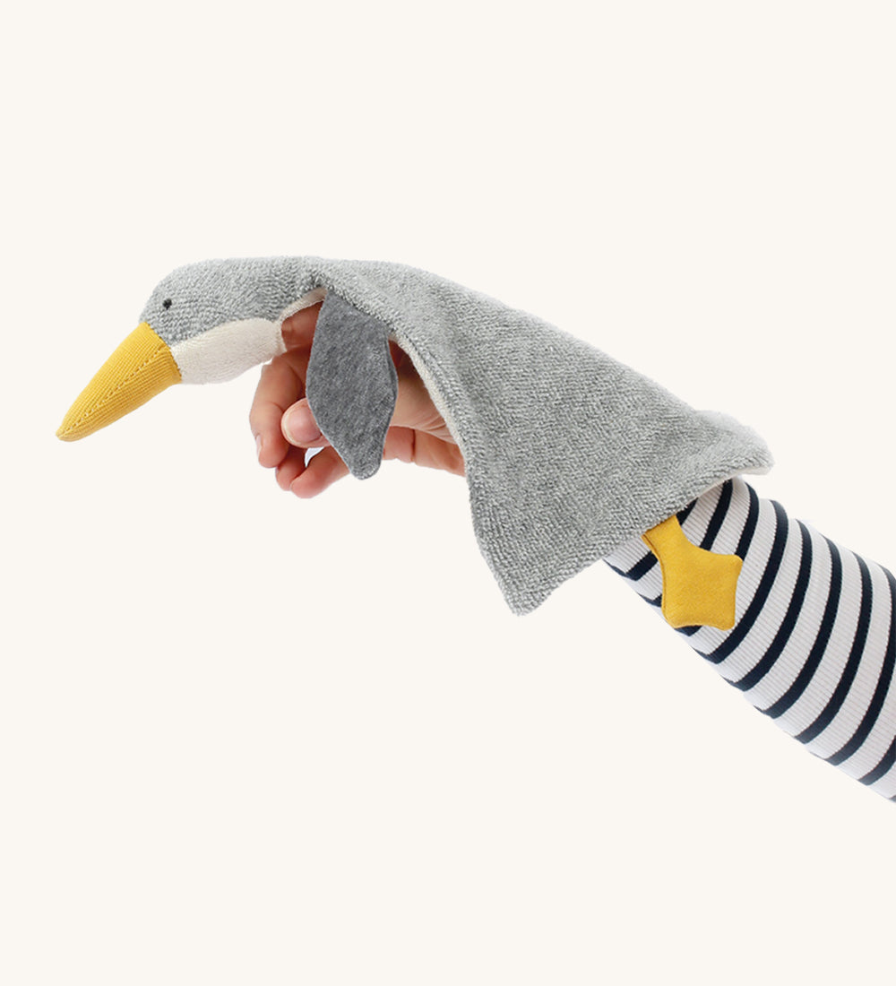 A person has the Nanchen Baby Comforter - Grey Goose resting on their arm, and underneath the head is a small hole to use the comforter as a finger puppet. The image is on a cream background