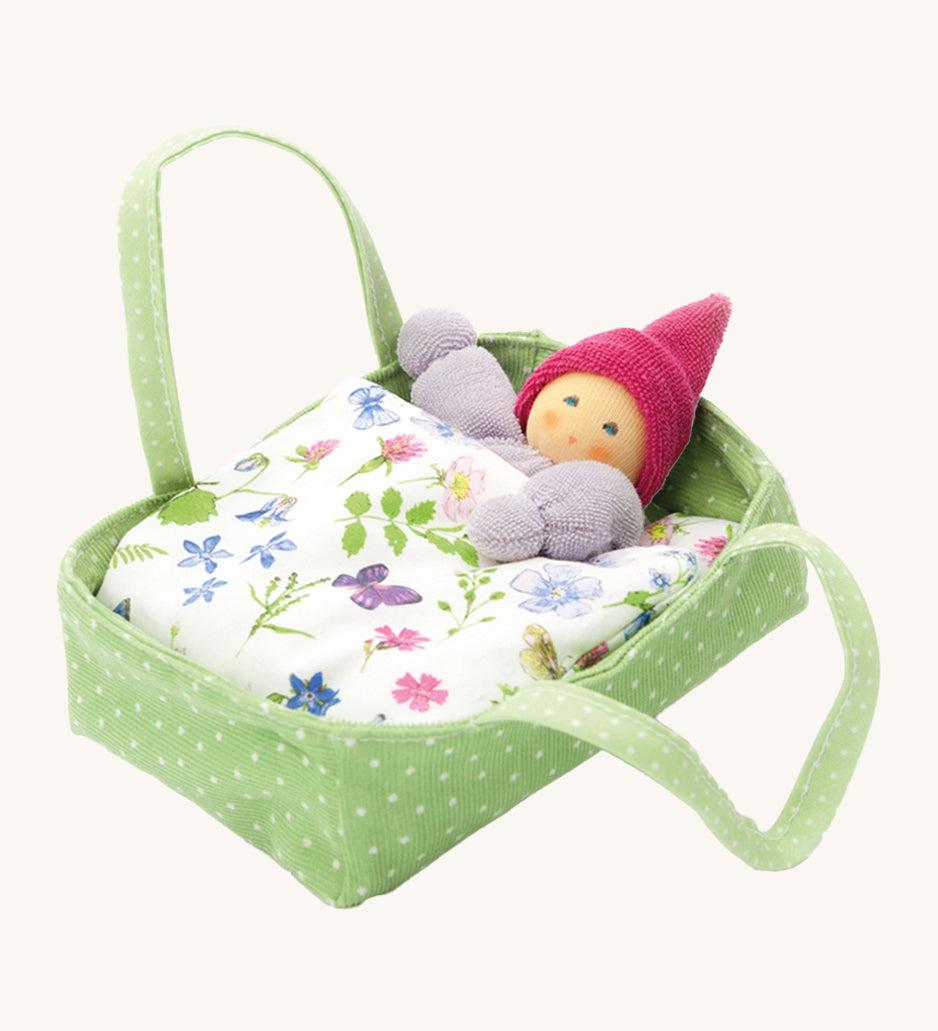 Nanchen Flower Bed doll with Carry Cot Toy, in green. A sweet little Waldorf doll which has been hand crafted in a terry material, is resting in a green and white spotted carry cot, under a beautiful botanical themed blanket. On a cream background