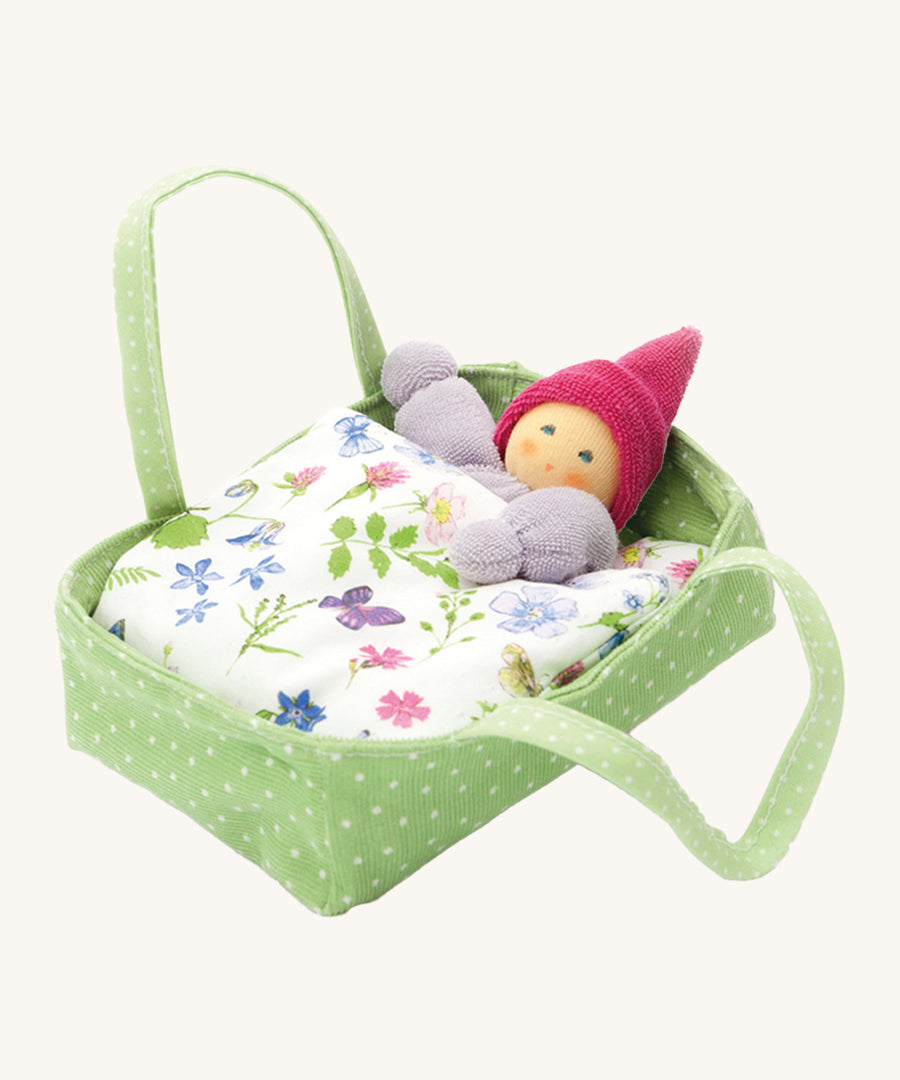 Nanchen Flower Bed doll with Carry Cot Toy, in green. A sweet little Waldorf doll which has been hand crafted in a terry material, is resting in a green and white spotted carry cot, under a beautiful botanical themed blanket. On a cream background