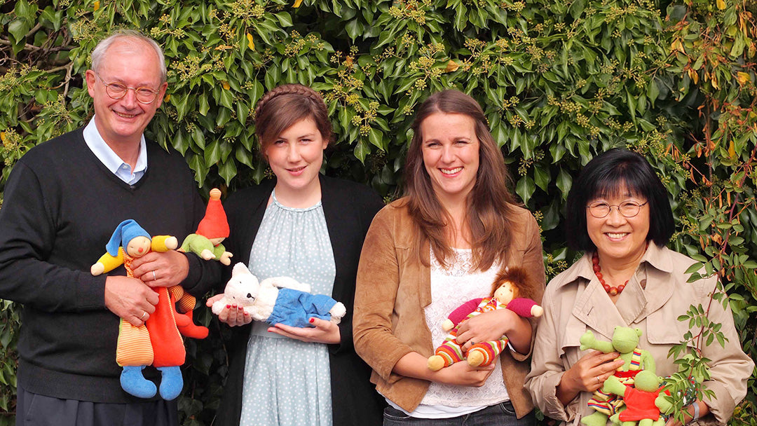 Nanchen Natur Owners in Germany stand by a green hedge.  They are carrying waldorf dolls in their hands 