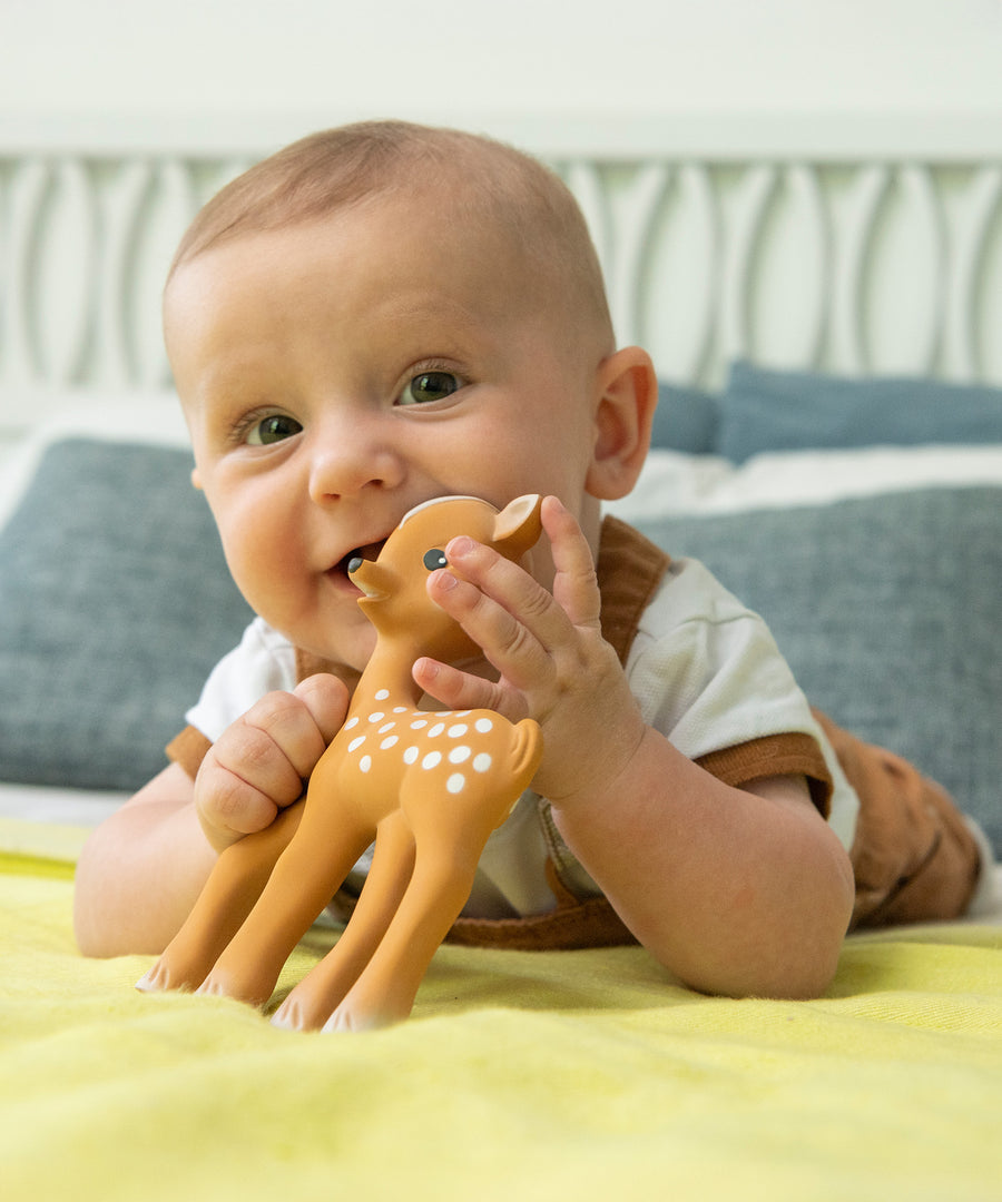 A child using Fanfan The Fawn as a teether whilst laying down. The child is happy and smiling whilst playing with the Fanfan The Fawn Natural Rubber Teething Toy