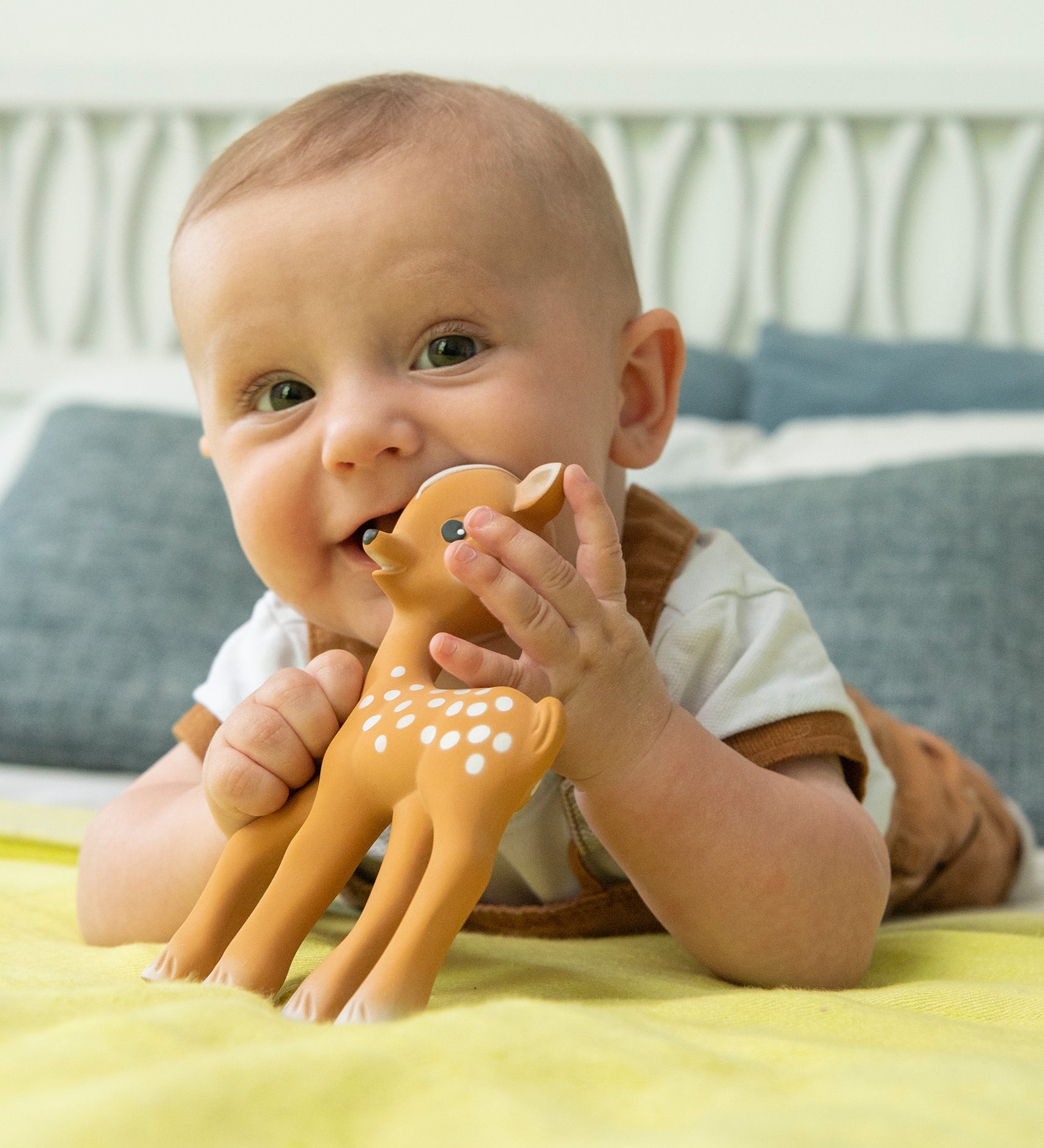 A child using Fanfan The Fawn as a teether whilst laying down. The child is happy and smiling whilst playing with the Fanfan The Fawn Natural Rubber Teething Toy