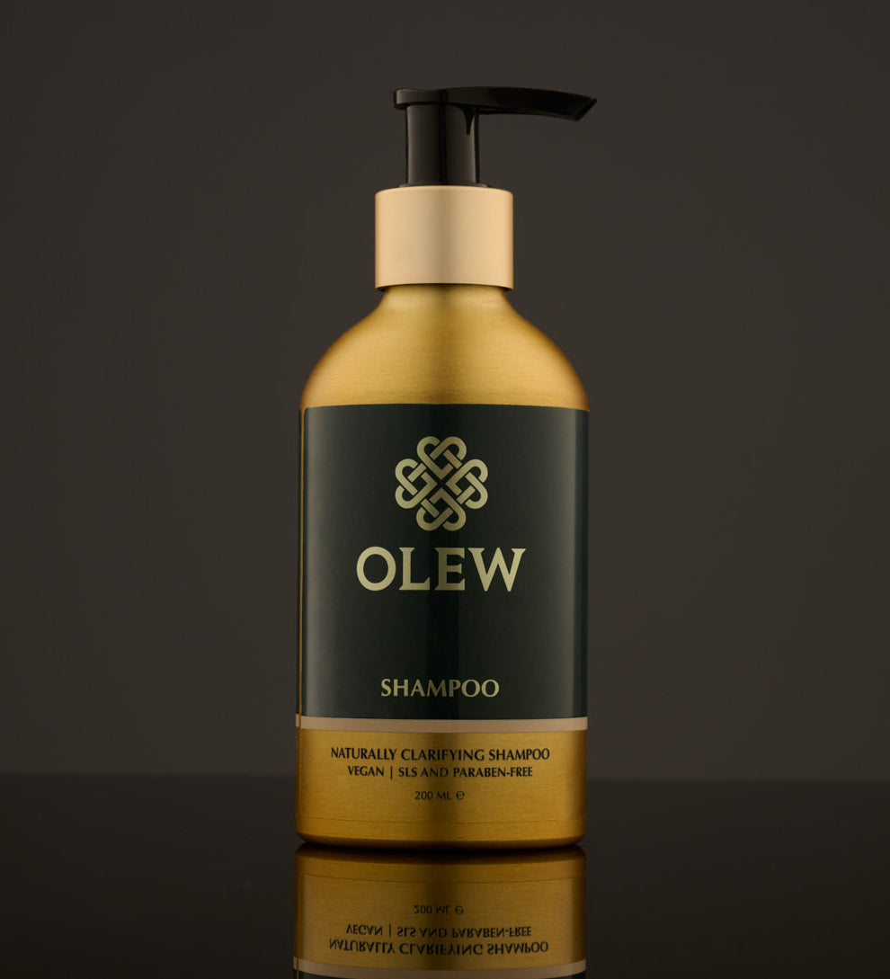 Olew Clarifying Shampoo, vegan haircare which is SLS and Paraben Free, in a gold and dark green bottle with a push down pump on top. The image is on a dark grey background