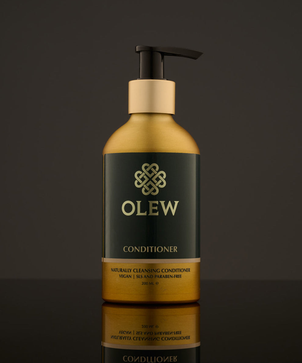 Olew naturally cleansing Conditioner, vegan haircare which is SLS and Paraben Free. In a gold and dark green bottle with a push down pump on top. The image is on a dark grey background