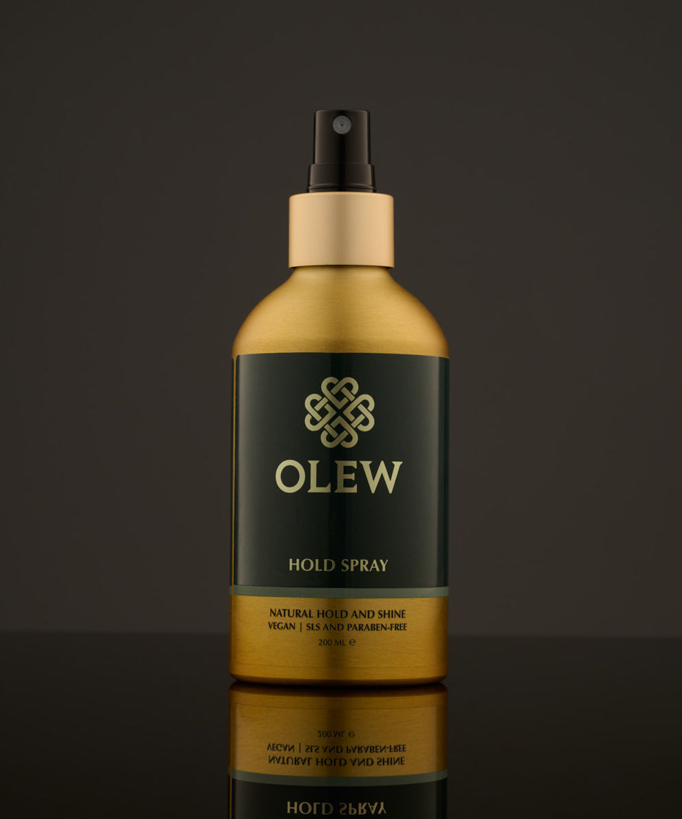 Olew Hold Spray - Curl Keeper, giving natural hold and shine. Vegan haircare which is SLS and Paraben Free, in a gold and dark green bottle with a spray mist pump on top. The image is on a dark grey background