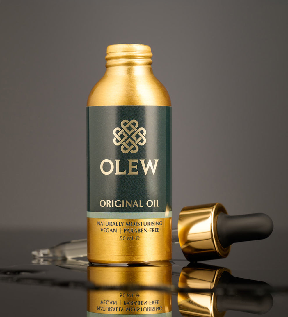 The Gold and black pipette top is laid behind the Olew Original Hair Oil bottle, on a dark grey background