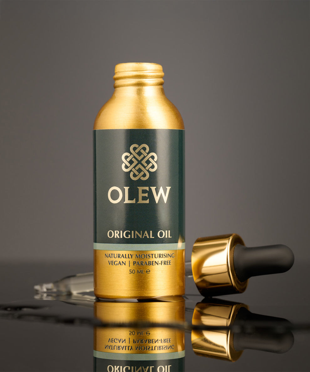 The Gold and black pipette top is laid behind the Olew Original Hair Oil bottle, on a dark grey background