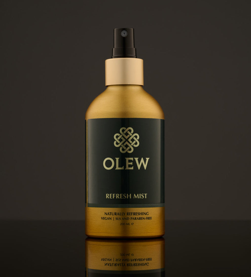 Olew Refresh Hair Mist, refreshing vegan haircare which is SLS and Paraben Free in a gold and dark green bottle, and a spray pump on top. The image has been taken on a grey background