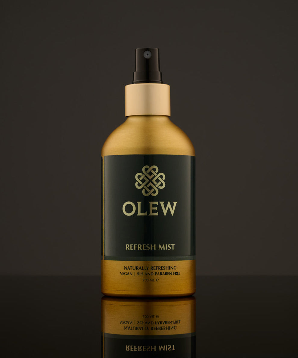 Olew Refresh Hair Mist, refreshing vegan haircare which is SLS and Paraben Free in a gold and dark green bottle, and a spray pump on top. The image has been taken on a grey background