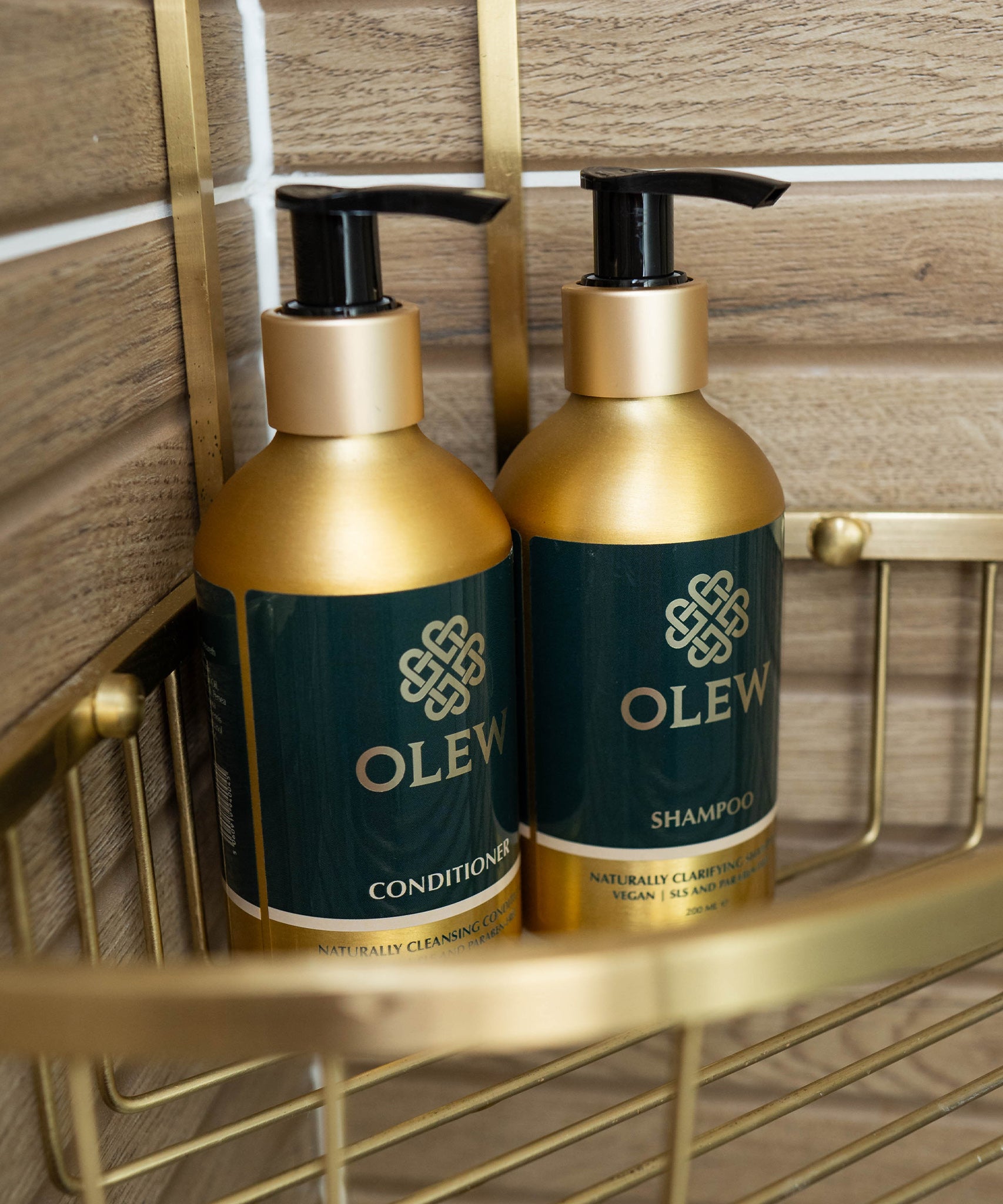 The Olew Conditioner and Shampoo in the gold and dark green bottles sat inside a gold shower caddy