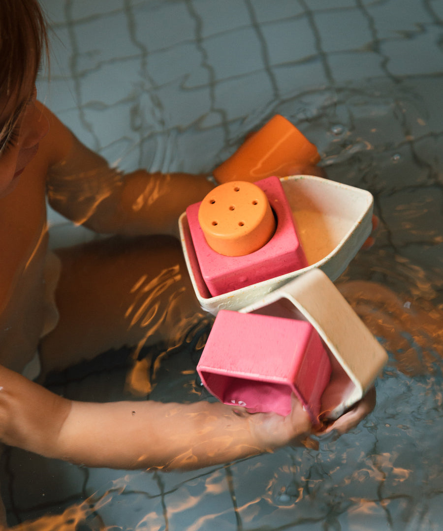 A child holding parts of the Oli & Carol Boat Bath Toy - Orange, in a bath