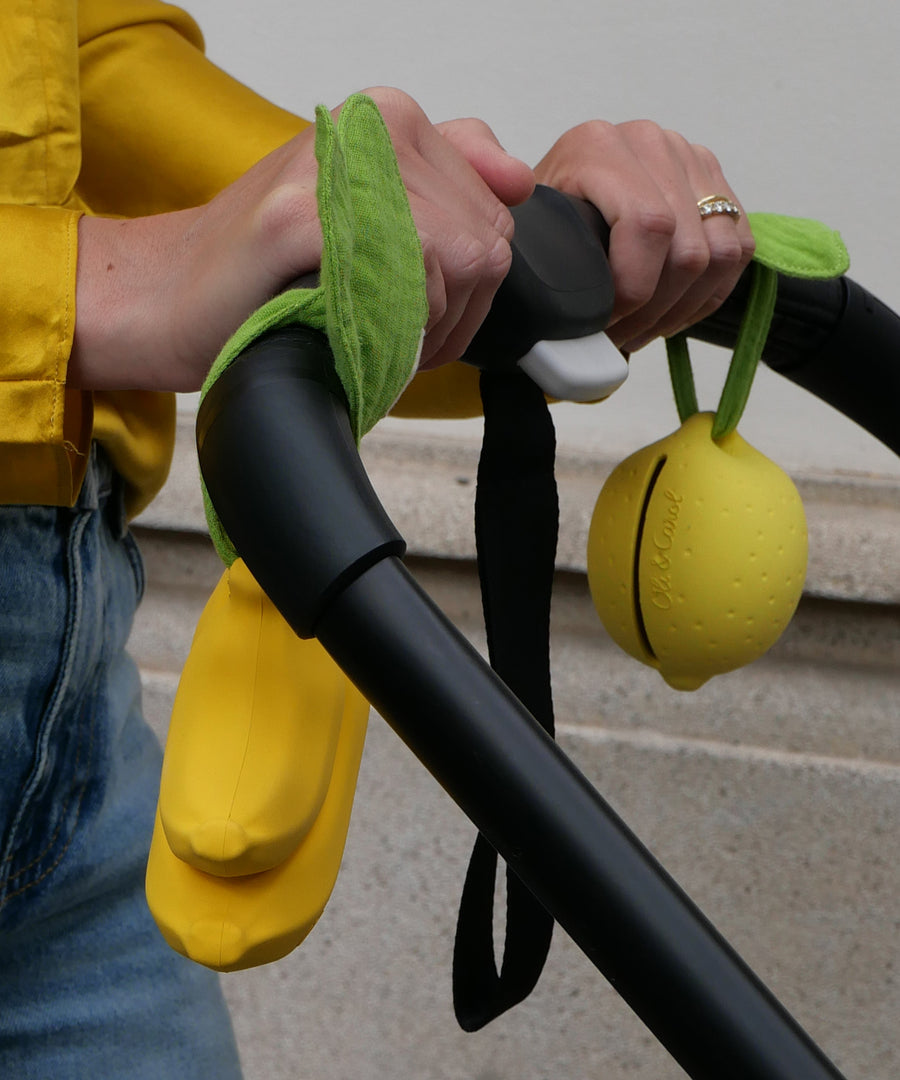 A closer look at the Lemon and Banana Pacifier Holder and Teething Toy, which have been tied onto a pram handle using the muslin cloth leaves on the top of the holder.