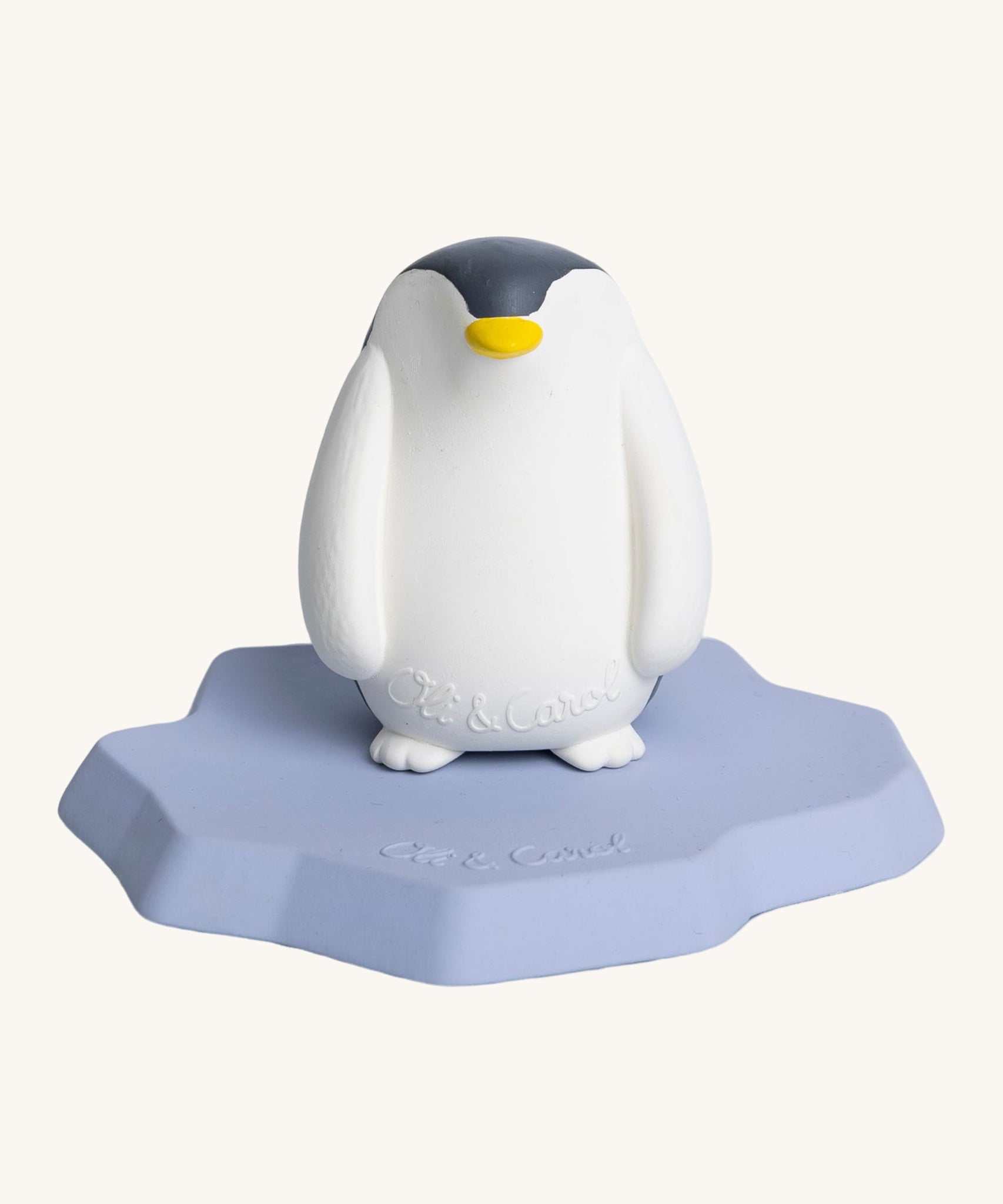 Oli & Carol Penguin Bath Toy. A bright white penguin, natural rubber bath toy is sitting on a flat, light blue/lilac ice berg on a cream background. The penguin is white and black, has a slightly textured body and has a yellow beak. 