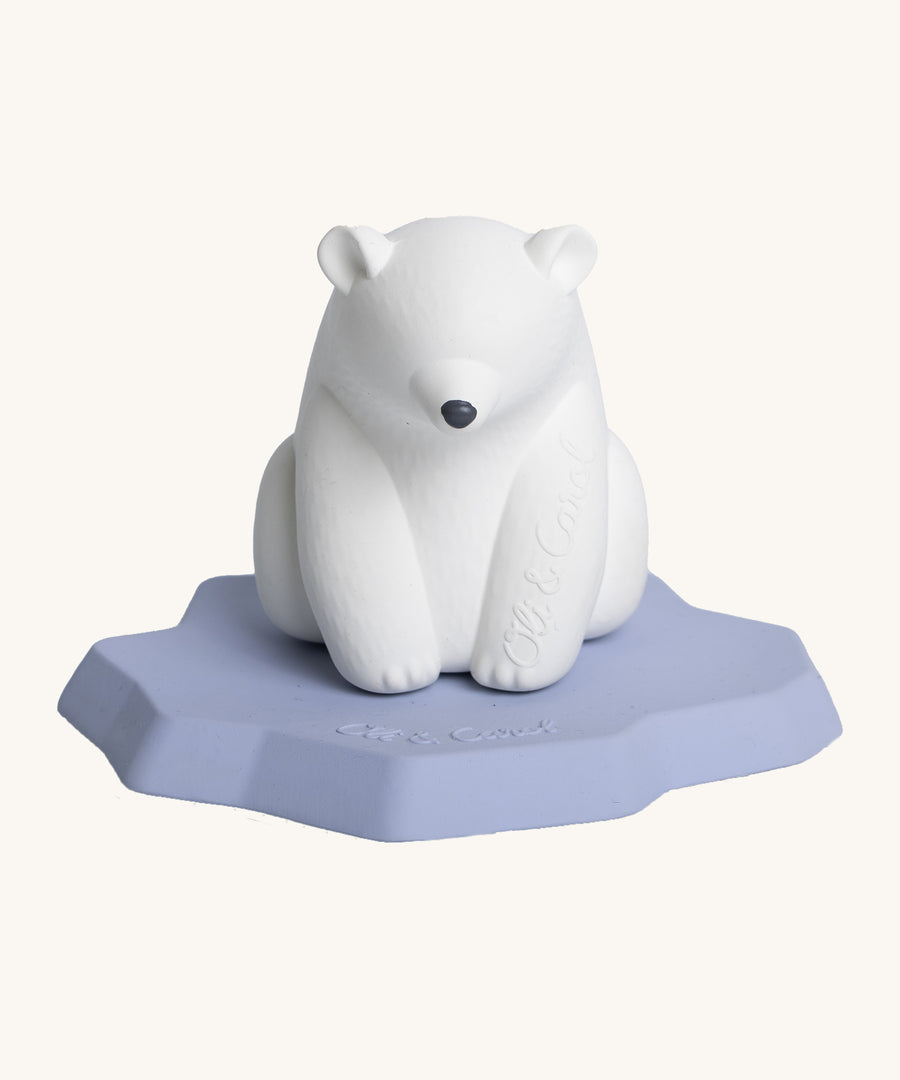 Oli & Carol Polar Bear Bath Toy. A bright white polar bear, natural rubber bath toy is sitting on a flat, light blue/lilac iceberg on a cream background. The polar bear is white, has a slightly textured body and has a black nose. 