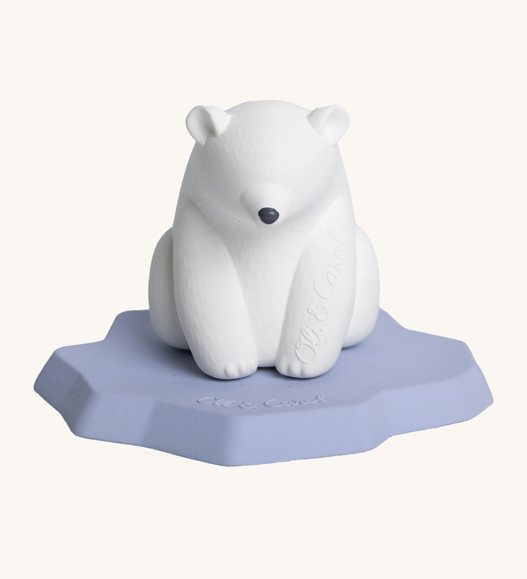 Oli & Carol Polar Bear Bath Toy. A bright white polar bear, natural rubber bath toy is sitting on a flat, light blue/lilac iceberg on a cream background. The polar bear is white, has a slightly textured body and has a black nose. 