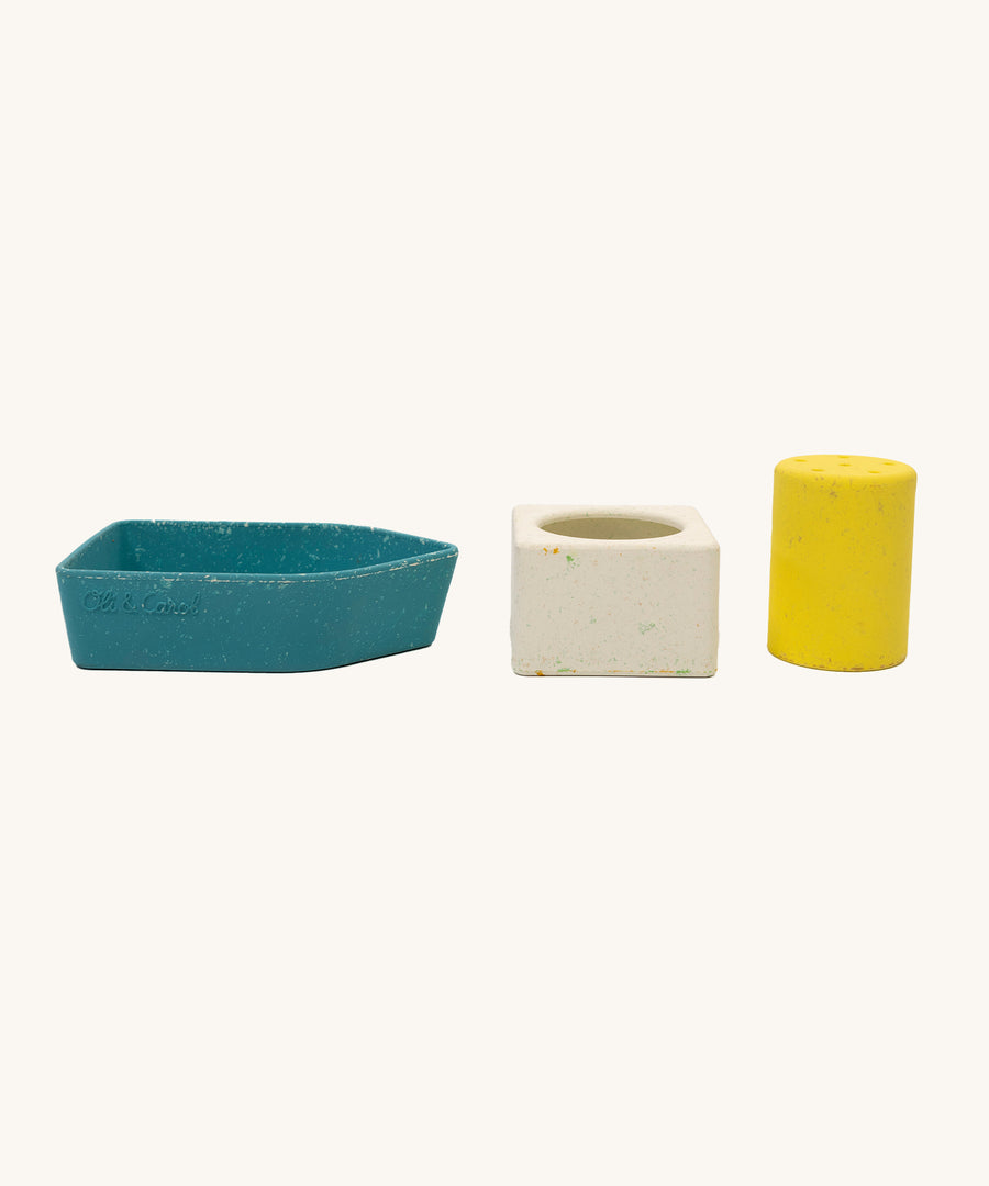 A blue boat base, a white square piece and a tall yellow cylinder from the Oli & Carol Boat Bath Toy - Yellow, all in a row together on a cream background