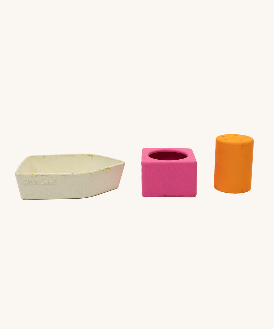 A white boat base, a pink square piece and a tall orange cylinder from the Oli & Carol Boat Bath Toy - Orange, all in a row together on a cream background