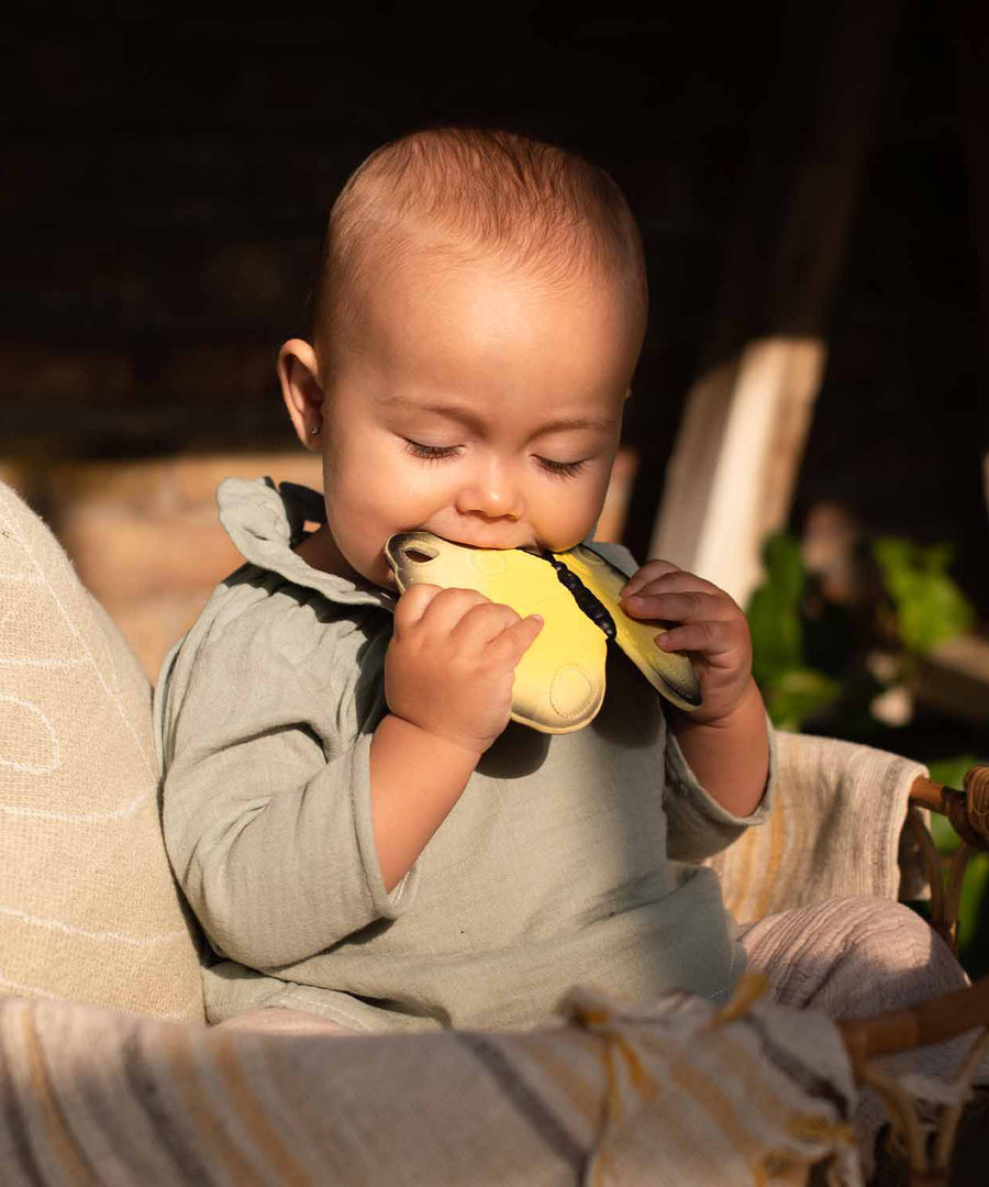 A child sat in the sun, chewing on the Oli & Carol Natural Rubber Teether - Katia The Butterfly