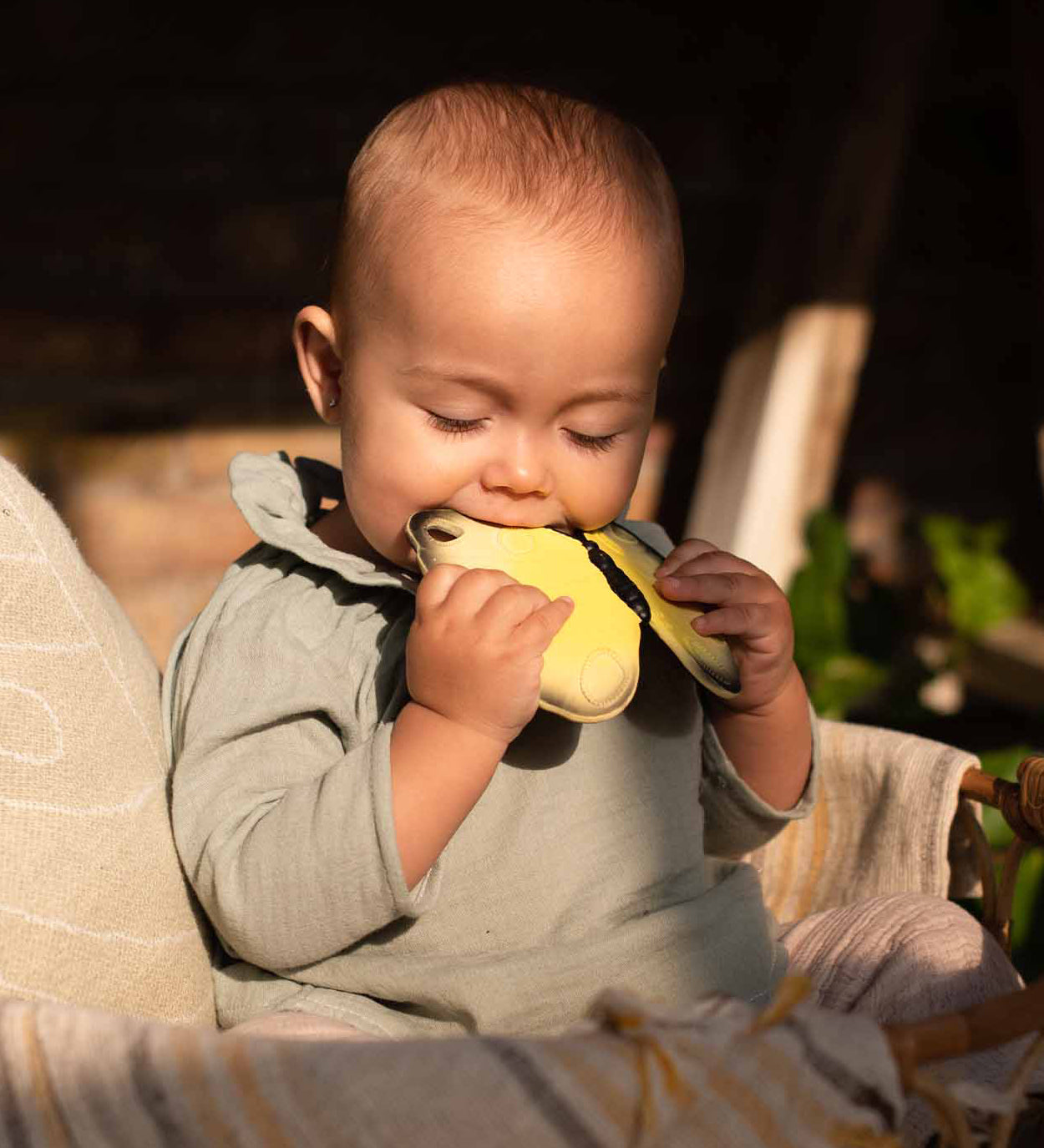 A child sat in the sun, chewing on the Oli & Carol Natural Rubber Teether - Katia The Butterfly