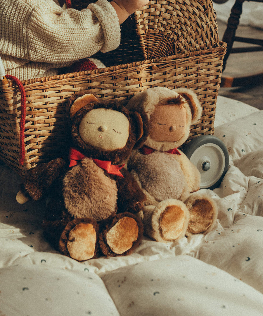 Olli Ella Cozy Dinkum Dolls Teddy Twiggy and Teddy Crumble together , sat in front of an Olli Ella Strolley Pram with a child sat inside.