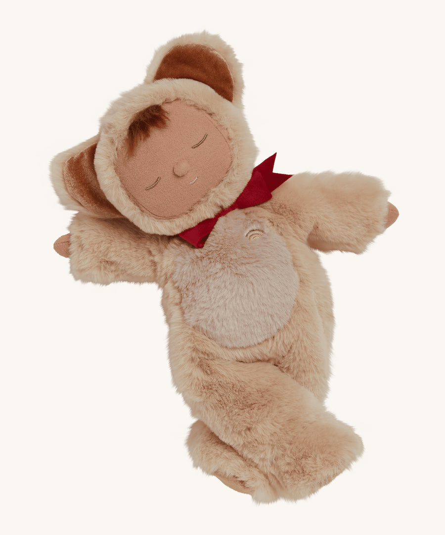 Olli Ella Cozy Dinkums - Teddy Crumble, is a super soft body teddy doll toy, with a soft fluffy Sand coloured outfit, with teddy ears and a red bow tie. The image is on a cream background