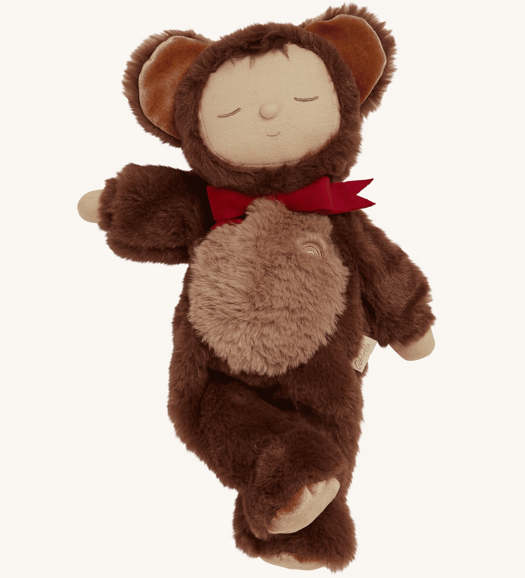 Olli Ella Cozy Dinkums - Teddy Twiggy is a soft body doll, with a soft and fluffy chocolate brown outfit which has a hood and teddy ears on top, and a red bow tie. The image is on a cream background.