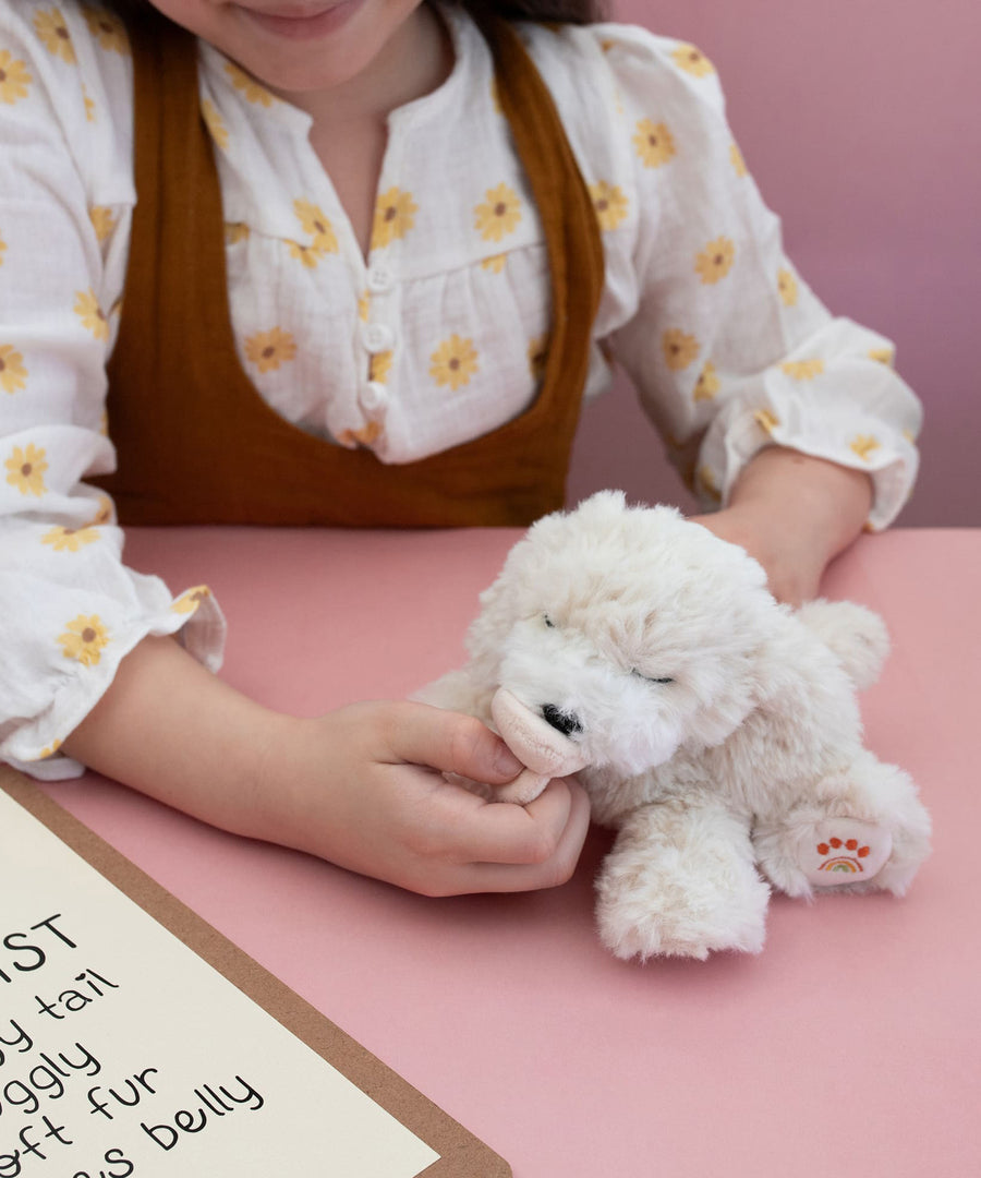 A child playing with the soft white Olli Ella Belle dinkum puppy.