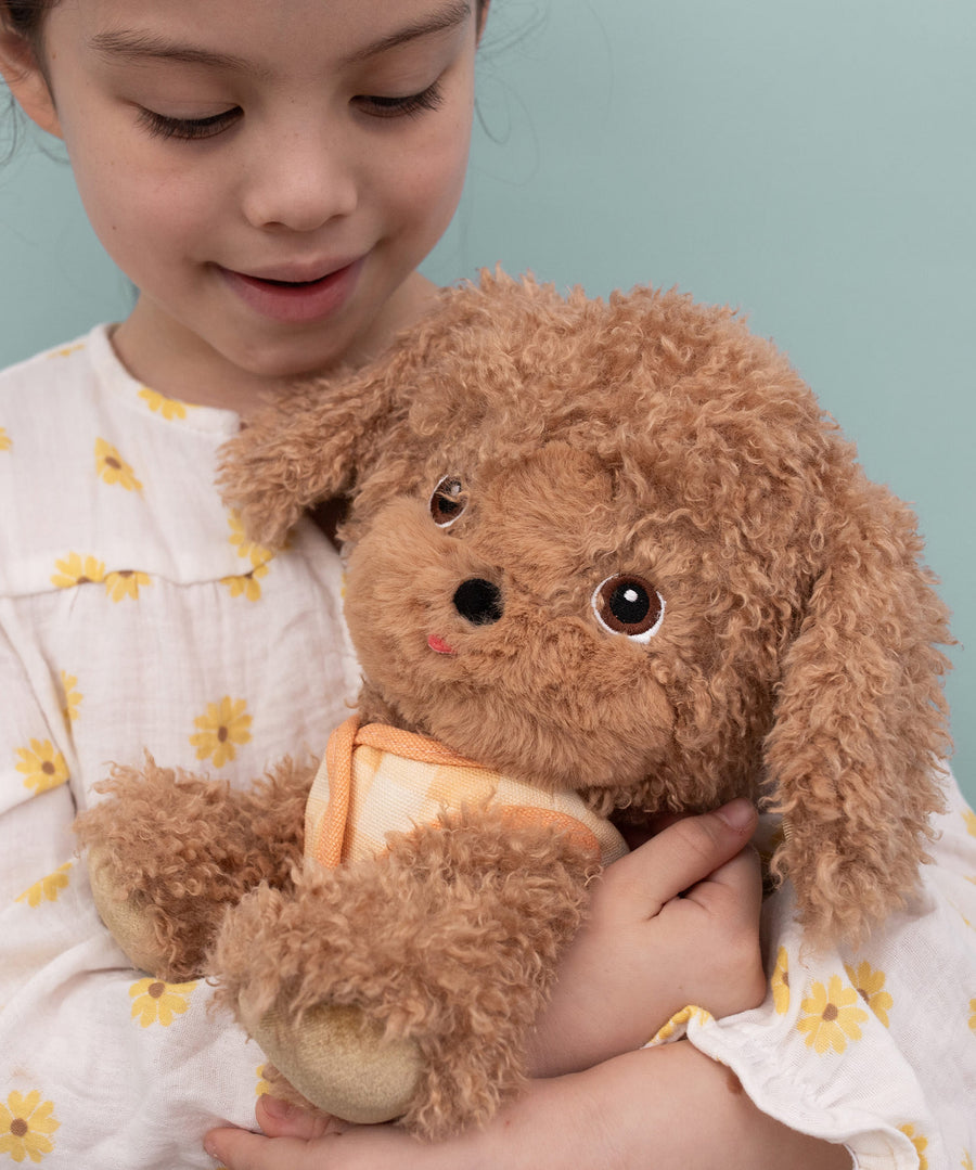 A child hugging the soft and fluffy brown Olli Ella Goldie dinkum dog.