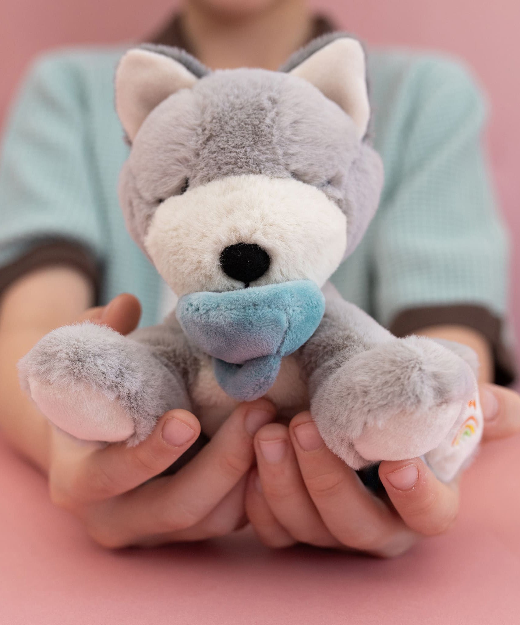 A child holding the soft grey and white Olli Ella dinkum puppy in their hands for scale