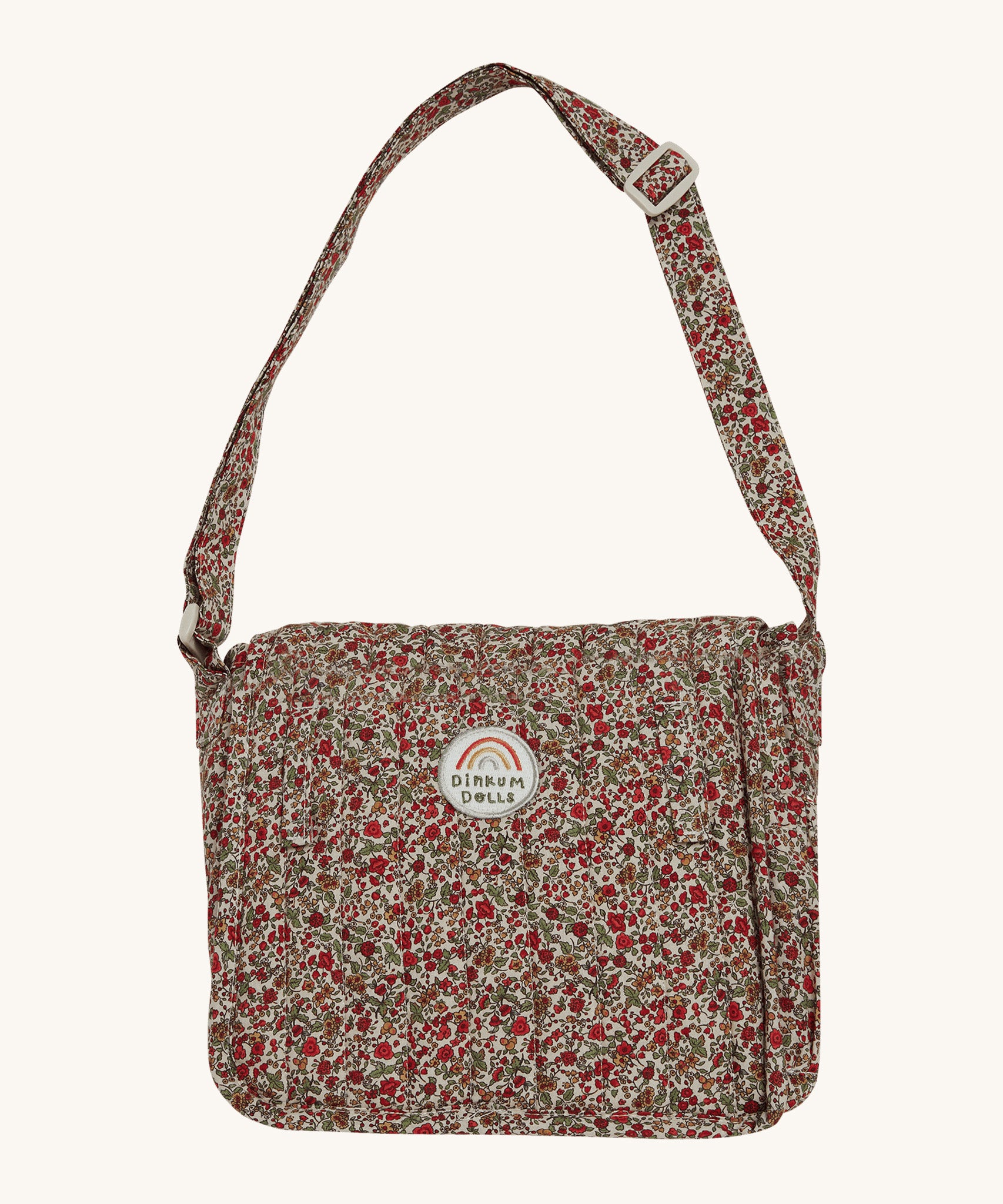 Olli Ella Carrie Convertible Changing Set - Garland. A beautiful floral print, cotton, changing bag for dolls and toys, with an adjustable shoulder strap. The changing bag coverts into a changing mat with the same floral print. The image is on a cream background