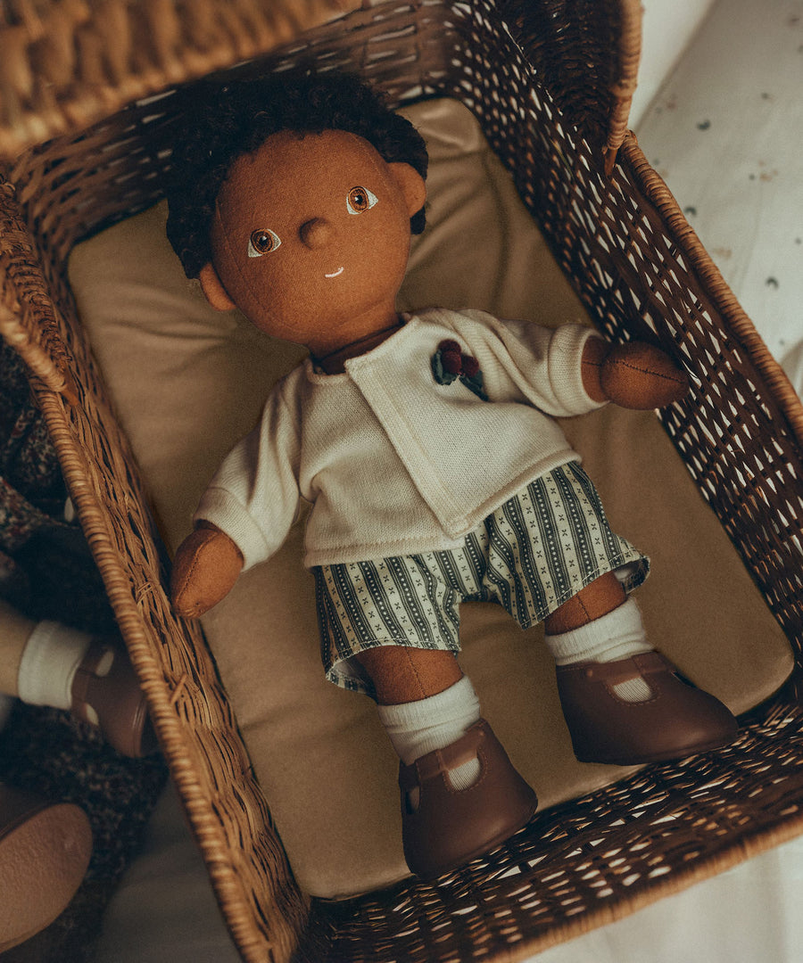 An Olli Ella Dinkum Doll, comfy in an Olli Ella Strolley, lying on the Champagne mattress. The Dinkum Doll wears the Olli Ella Dinkum Doll Holiday Outfit Set, white sock and brown shoes.