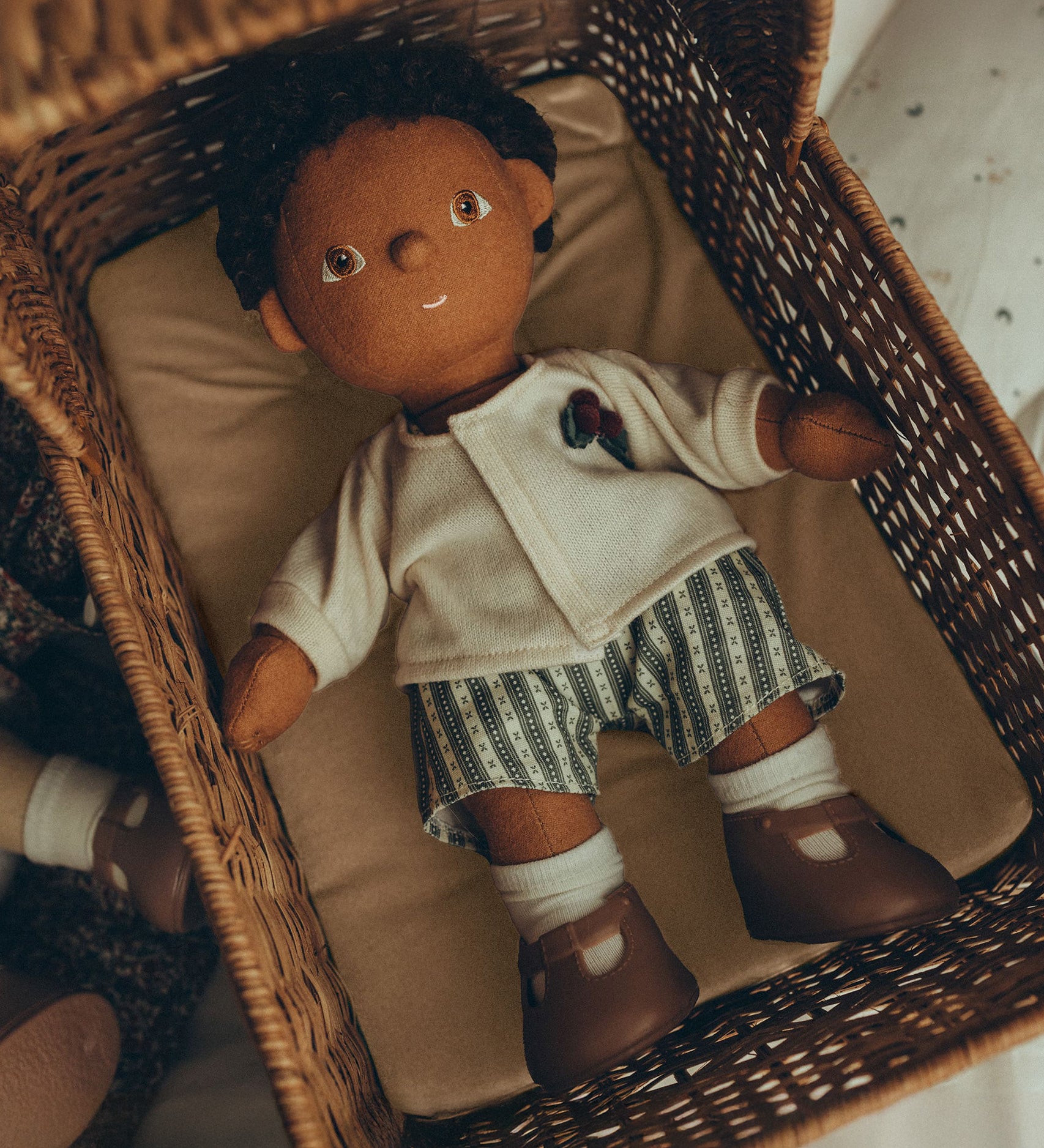 An Olli Ella Dinkum Doll, comfy in an Olli Ella Strolley, lying on the Champagne mattress. The Dinkum Doll wears the Olli Ella Dinkum Doll Holiday Outfit Set, white sock and brown shoes.