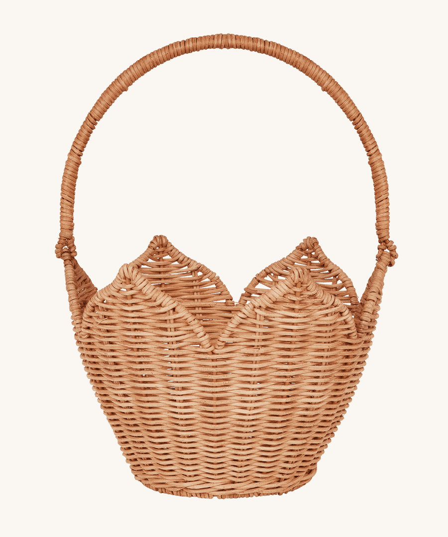 Olli Ella Rattan Poinsettia Carry Basket is a beautiful scalloped, handwoven, rattan basket in a light brown, with a carry handle. The basket is on a cream background.