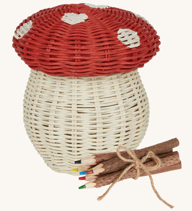 An Olli Ella Porcini mushroom shaped Basket with a red spotted lid, and wooden twig colouring pencils wrapped together with string next to it pictured on a cream background