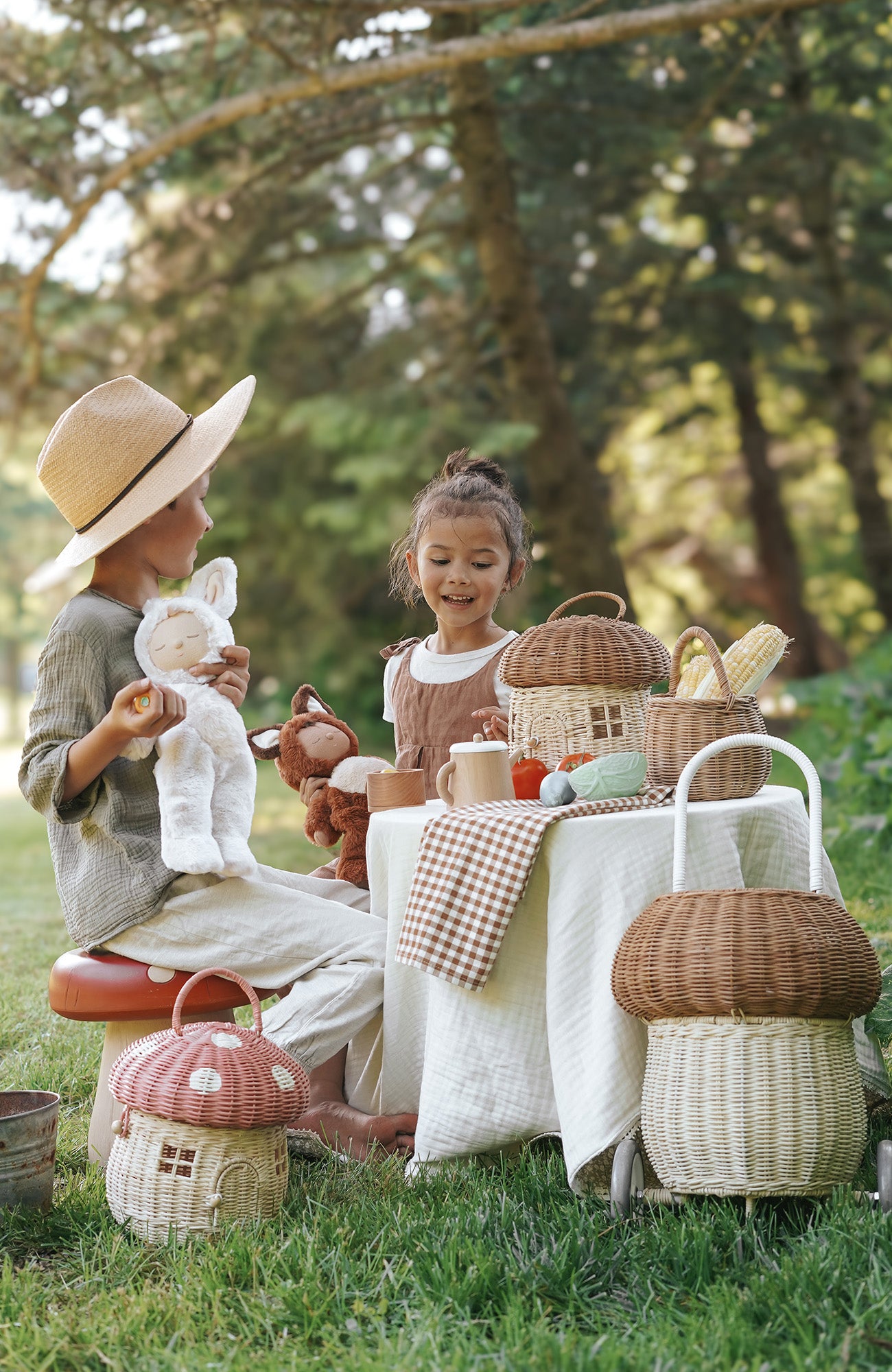 Siblings playing in the forest with Cozy Dinky dolls, surrounded by Olli Ella baskets