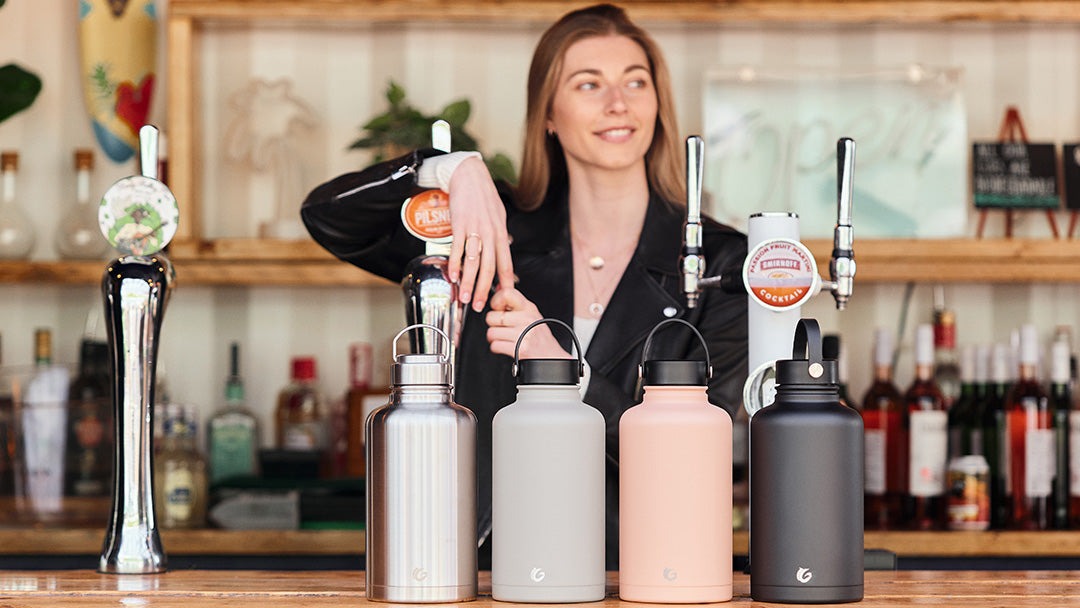 Woman behind a bar, with four One Green Bottle stainless steel bottles ready to have drink poured into them