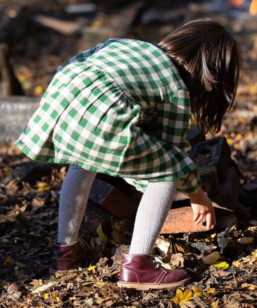 A child bending down to play with crunchy autumn leaves, wearing the Little Green Radicals Check Pocket Dress - Fern Green. The image shows the back of the dress.