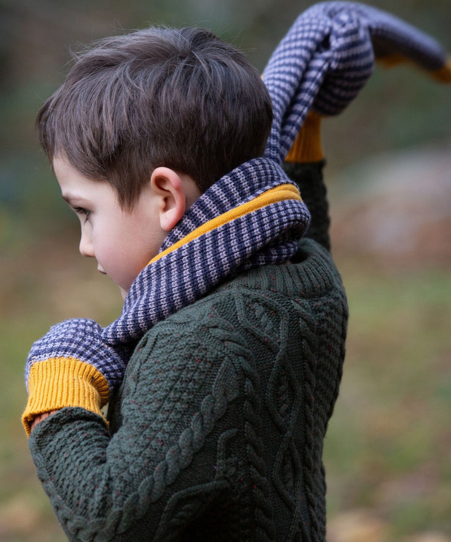 A child putting on the Dreamy Blue knitted scarf on their neck. The child is also wearing the Dreamy blue stripe mittens