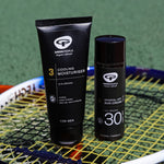 The Green People Sports+ Sun Cream and the Green People Cooling Moisturiser are both stood on top of a tennis racket, with a green playing field in the background