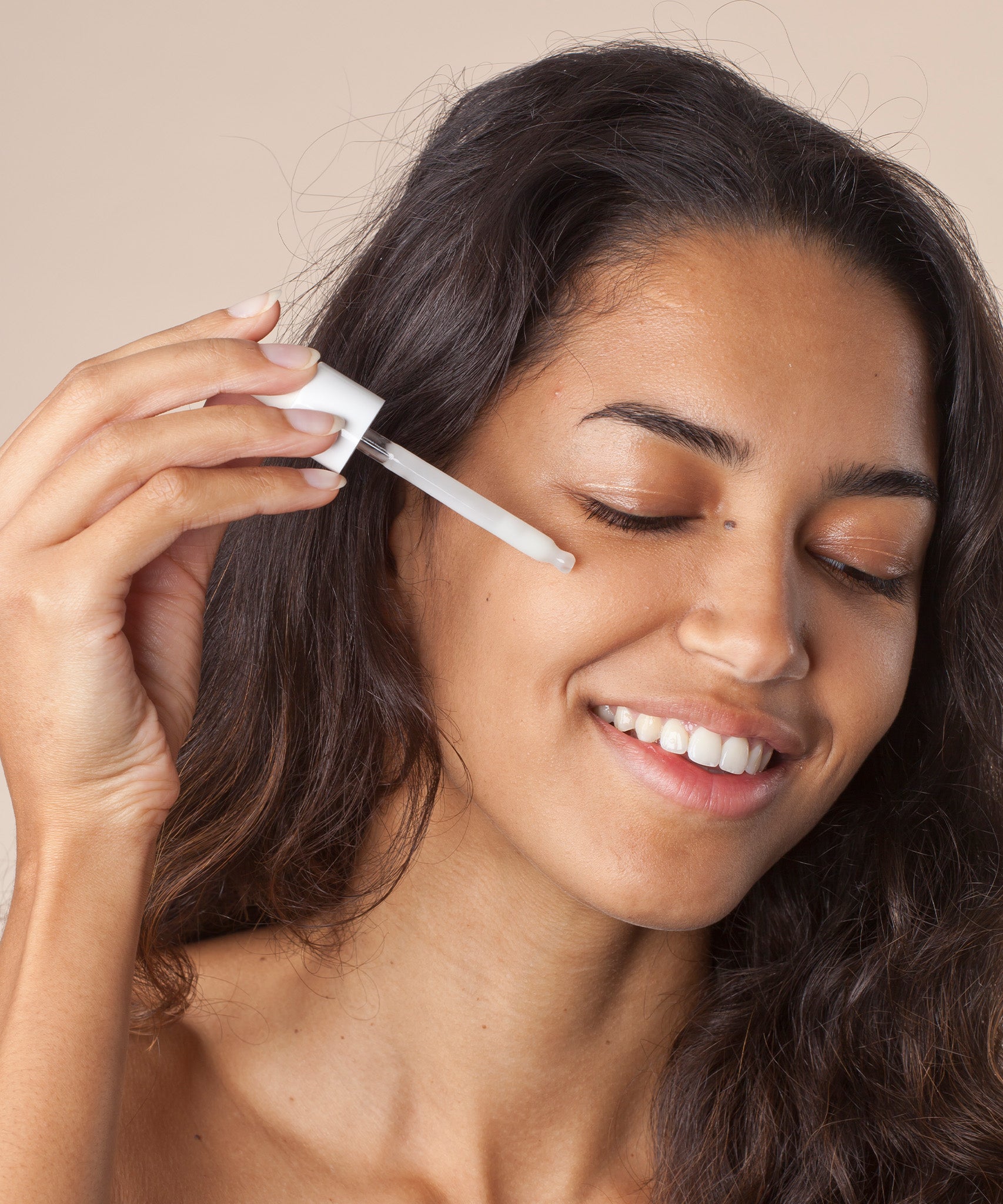 A person applying the Green People Nordic Roots Hyaluronic Booster Serum -onto their face. The image shows the silky, white serum in its lid dropper 