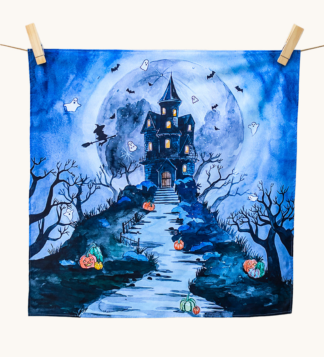 An organic play cloth with a fabulous spooky and Halloween print. A haunted manor on top of a steep hill side with stairs leading up to the door, has cute ghosts, bats and a witch circling around it. Behind the manor, is a large, full moon, and pumpkins outline the stairs and path to the manor