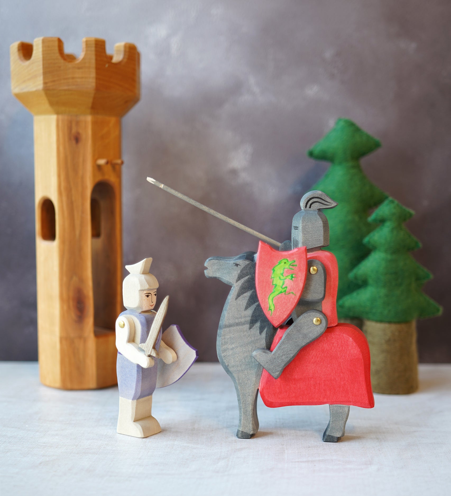 The Ostheimer Wooden Blue Standing Knight Figure standing next to the Black Knight and Horse set with trees and a wooden tower in the background.