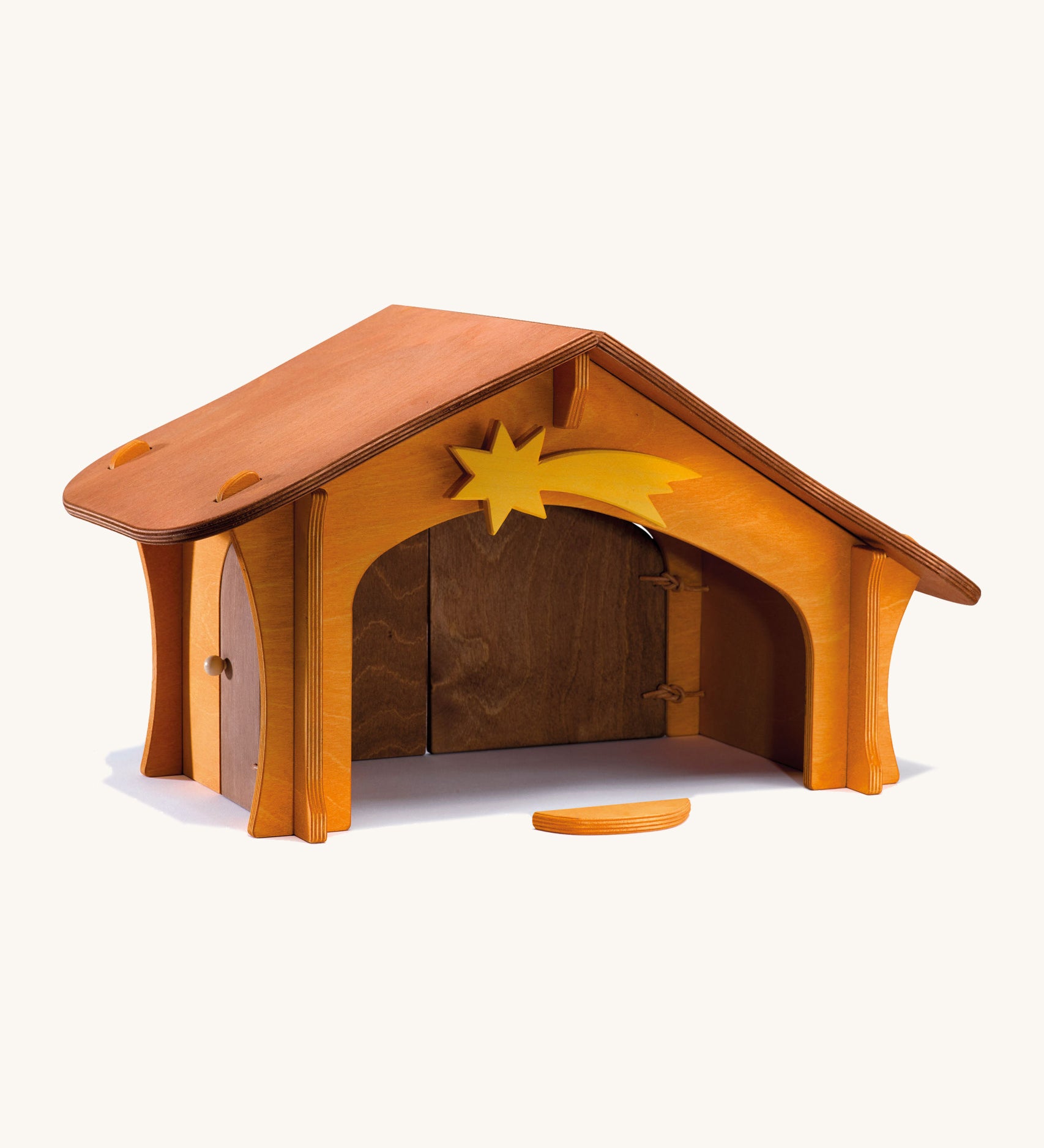 A wooden Ostheimer stable with a wooden shooting star on the top and a wooden bird perch in front of the stable on a cream background.