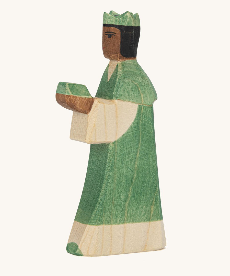 A Ostheimer wooden king figure wearing a green gown and a green crown on his head on a cream background.