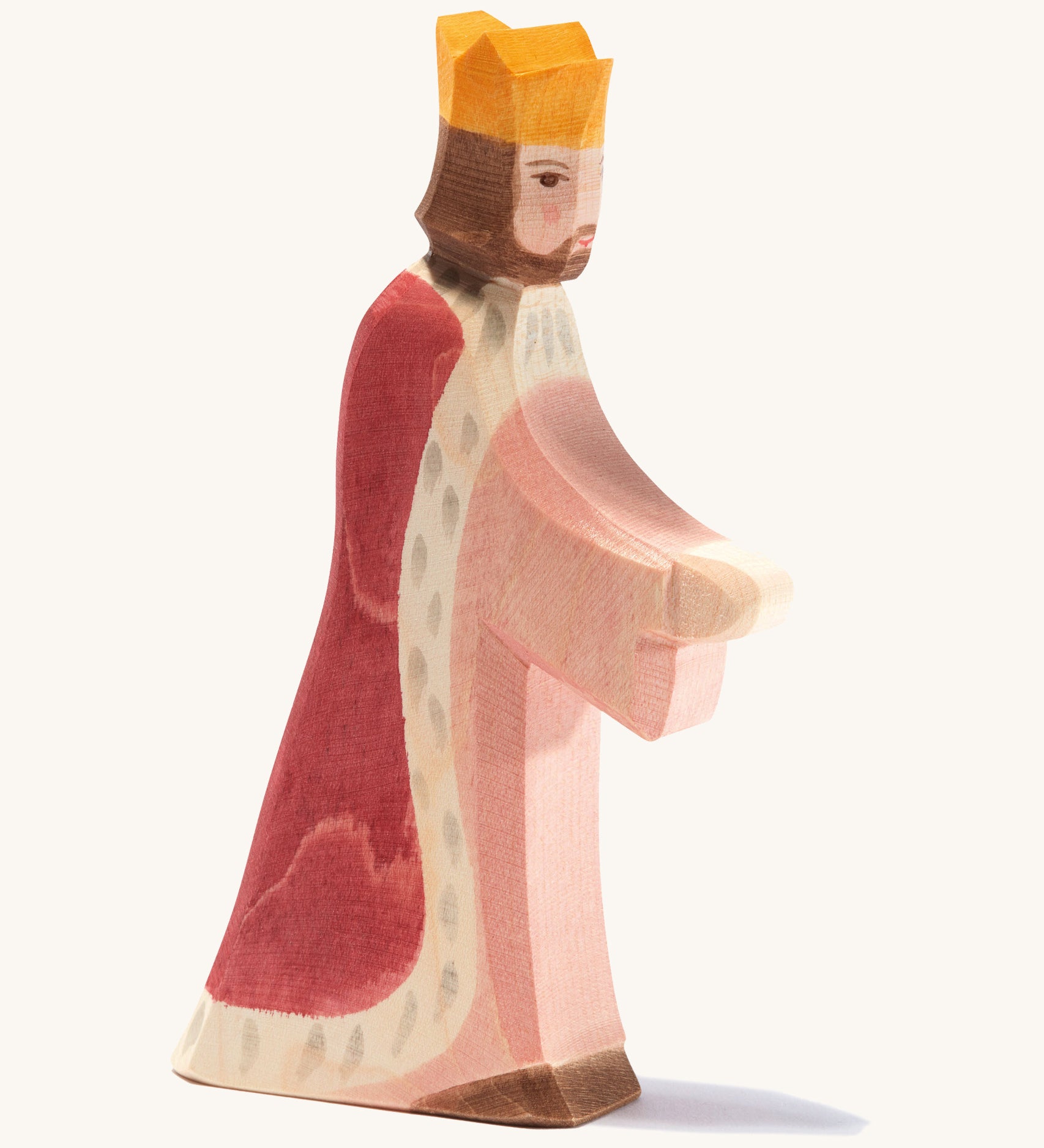 A Ostheimer wooden king figure wearing a pink gown and red cloak with a gold crown on his head on a cream background.